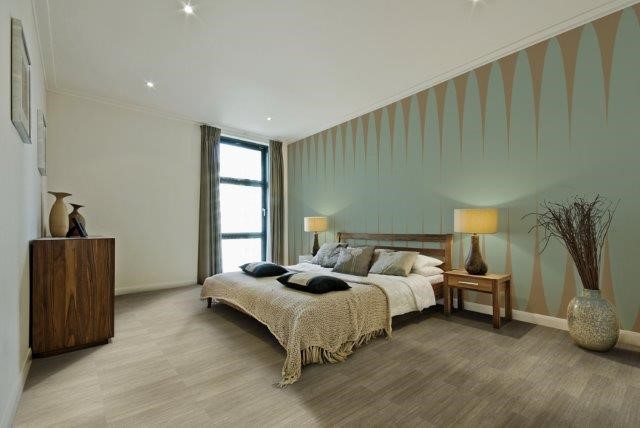 quarto moderno com cama de casal no centro, piso vinilico marrom claro e uma parede verde agua e detalhes em marrom