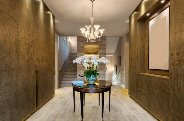 corredor com paredes marrom, uma mesa central com um vaso com flor no centro e piso vinilico marrom claro no chão